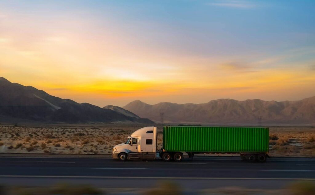 Semi truck hauling a container on a desert highway at sunset